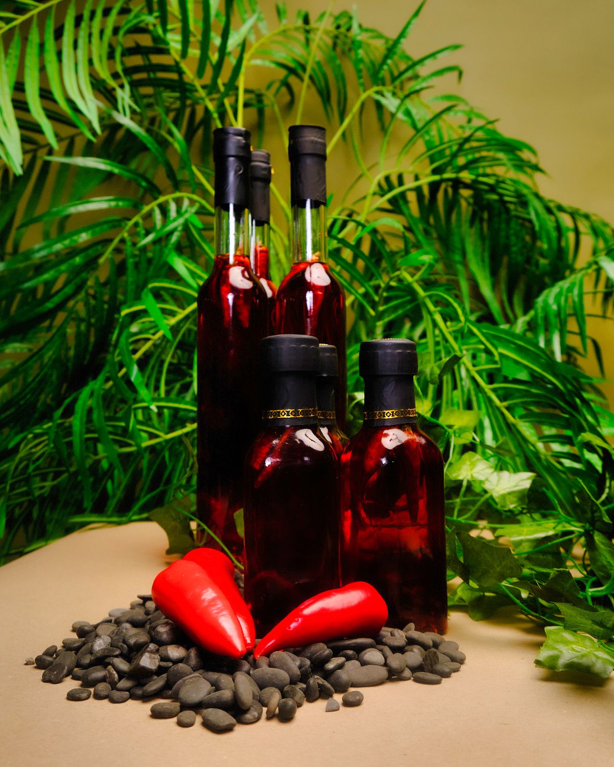 Red wine bottles and chili peppers arranged with coffee beans and tropical leaves in still life composition.