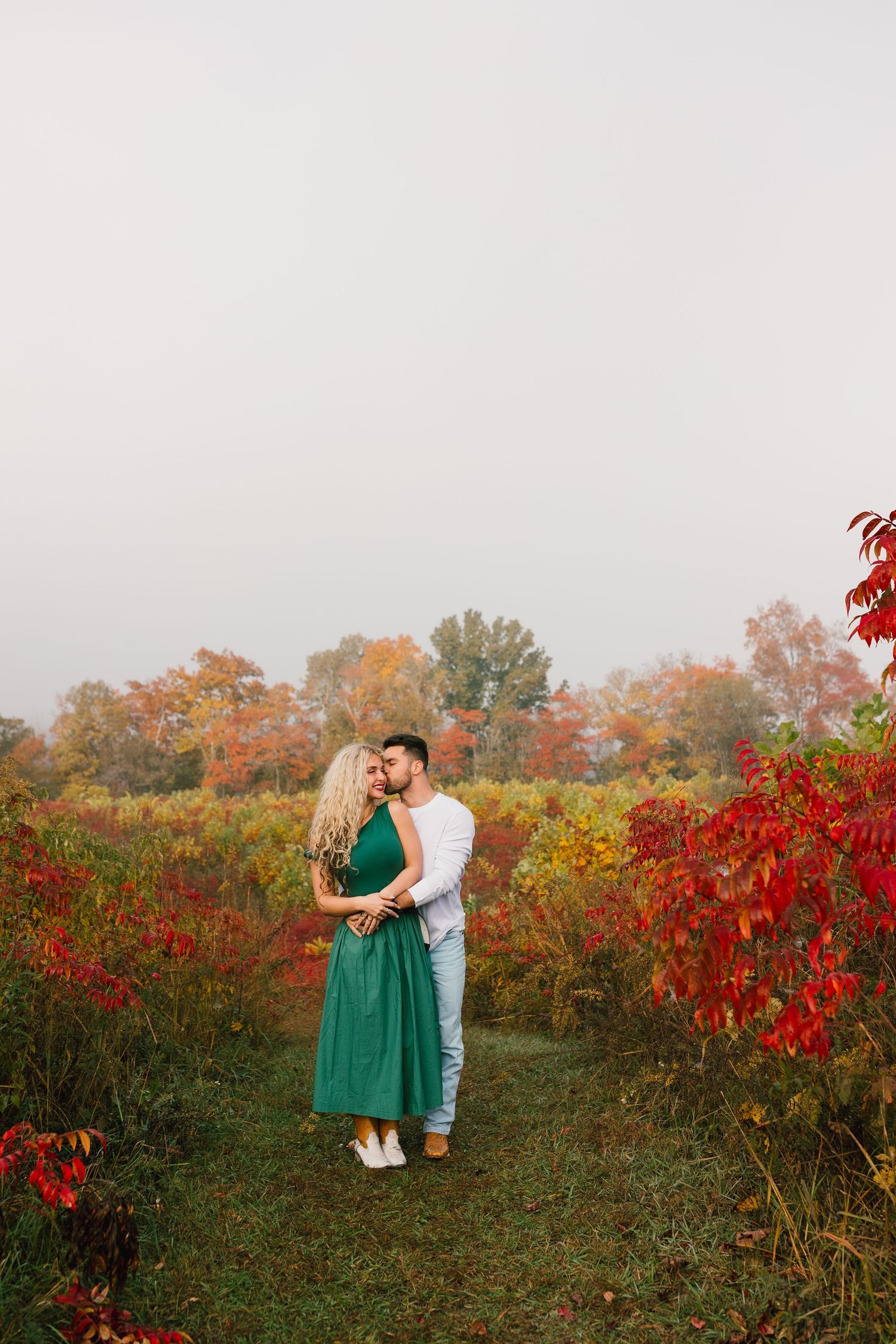 Couple embracing in a field of vibrant red autumn foliage at sunset.