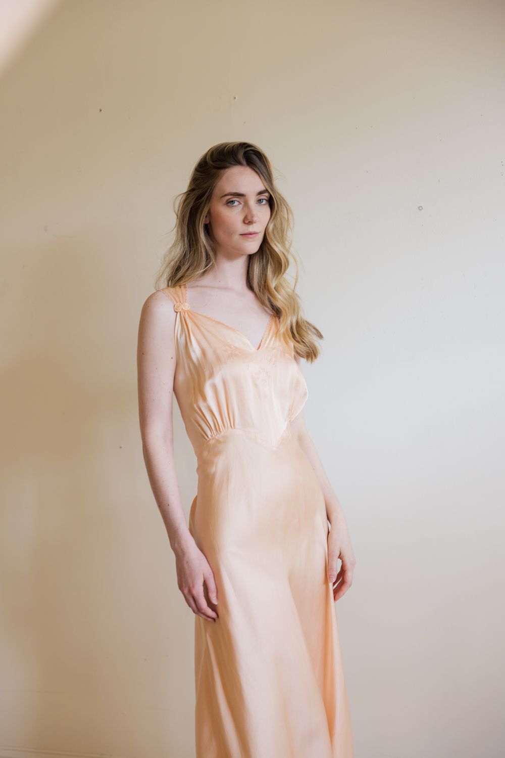 Woman in elegant peach satin slip dress with V-neckline, posing against a neutral background.