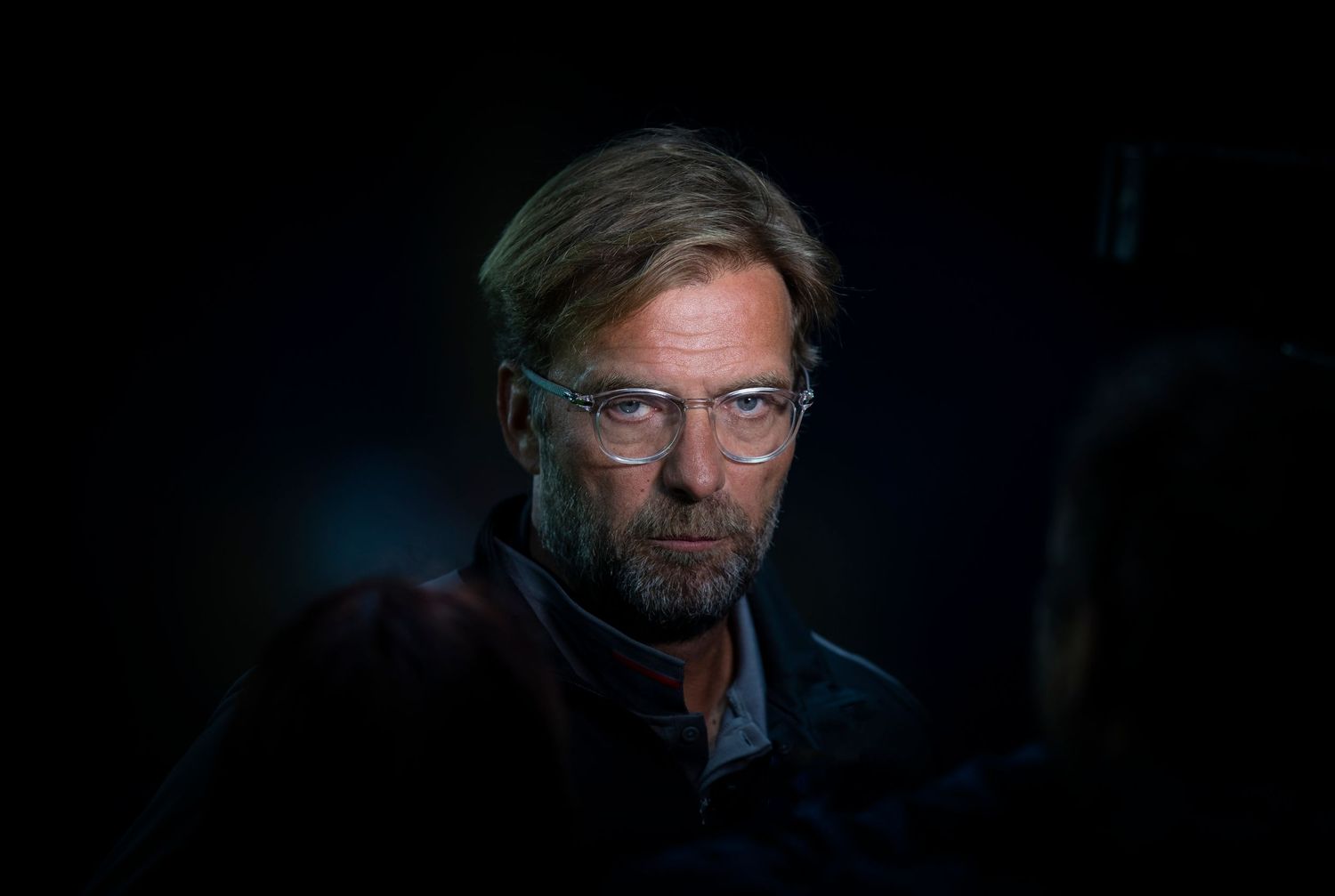 A man with glasses and a beard photographed in dramatic low-key lighting against a dark background.