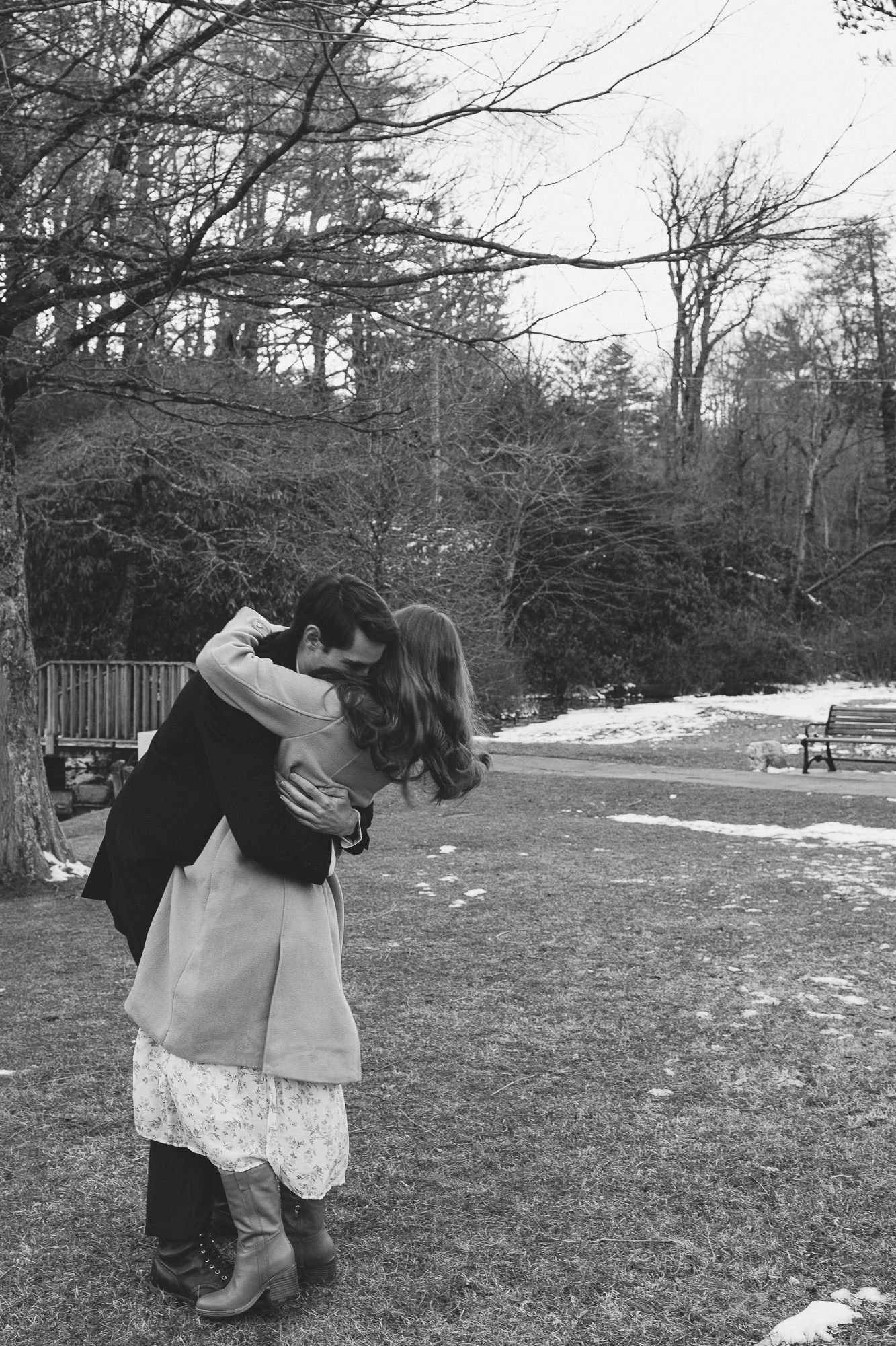 A romantic winter scene in a park with a couple embracing near bare trees and patches of snow. Château des  Fleures Wedding Photographer