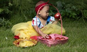 Infant dressed as Snow White looking at apple.