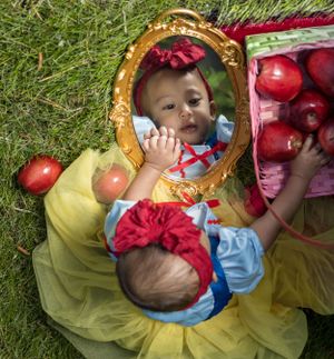 Infant dressed as Snow White looking in mirror.