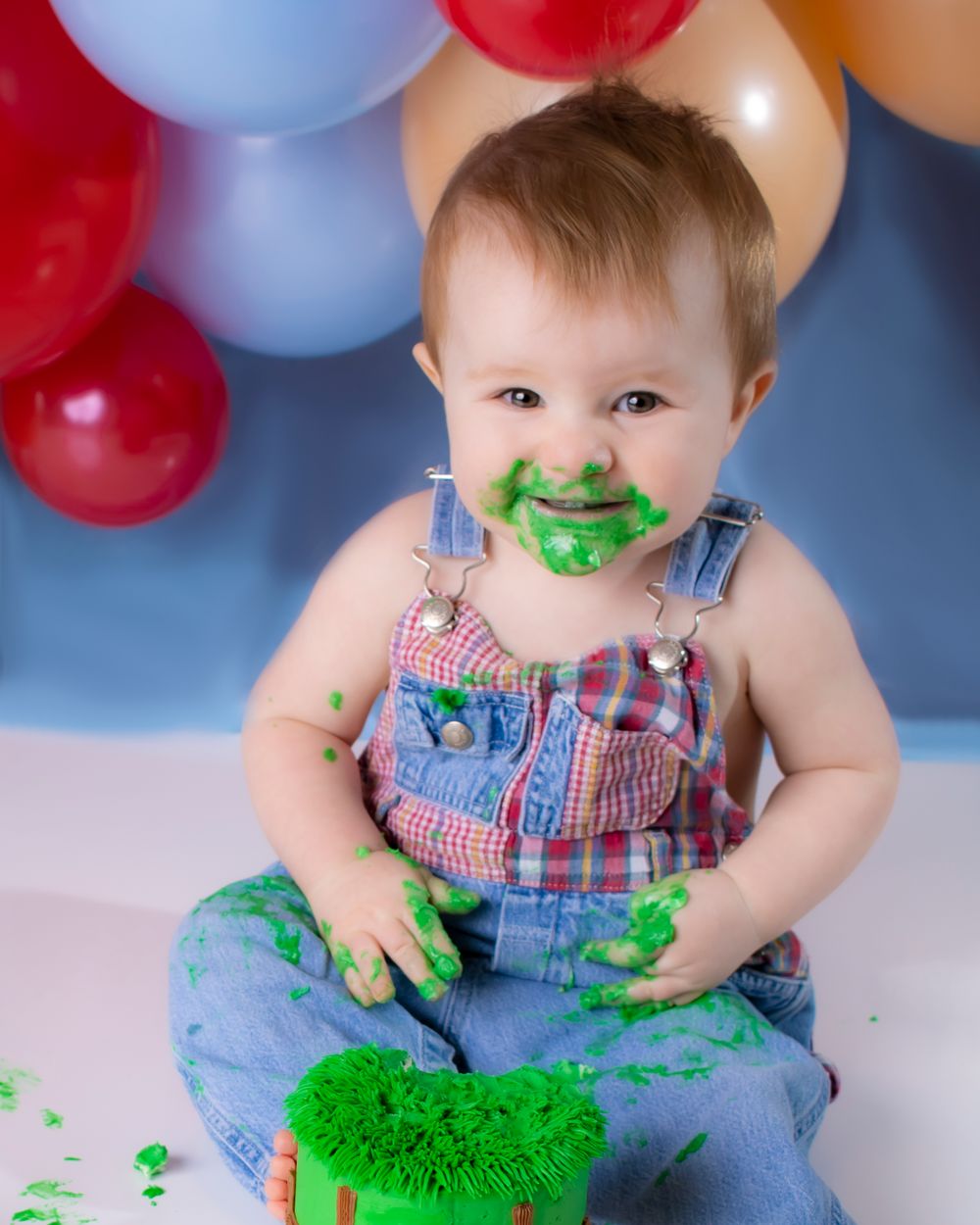A baby boy covered in green frosting enjoys a small cake