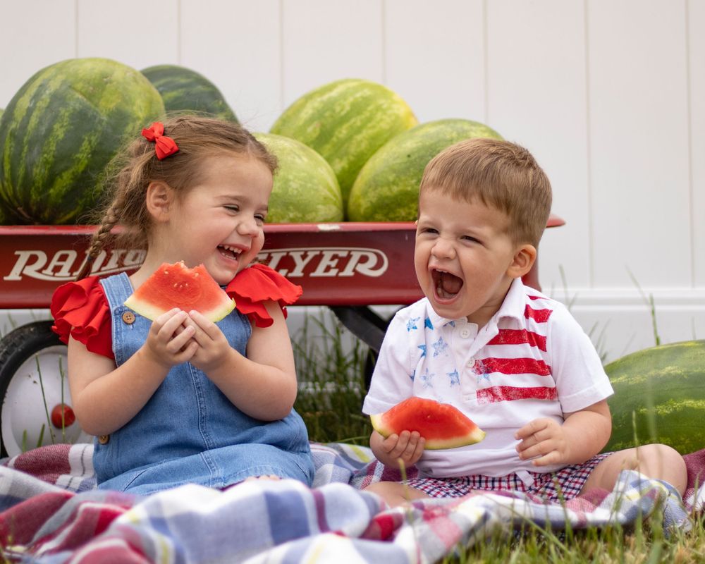 Two toddlers smile and laugh eating watermelon