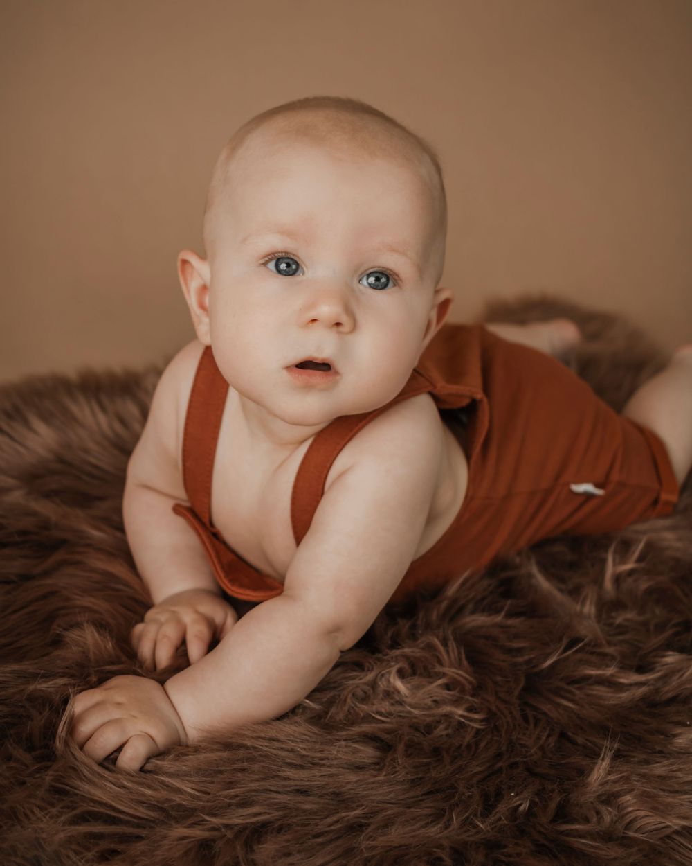 A baby boy lies on his stomach while looking over his shoulder