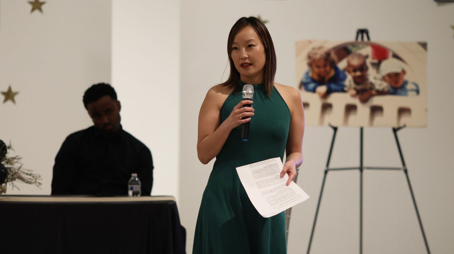 Speaker in a green dress presenting at an indoor event venue.
