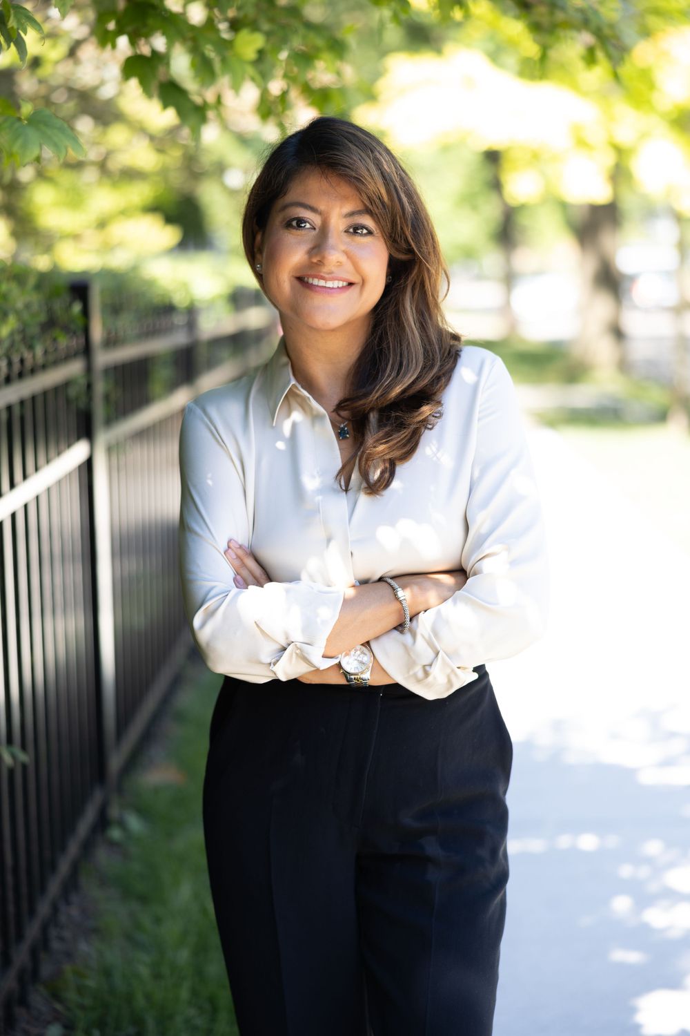 Confident young professional woman in white blouse posing outdoors with arms crossed.