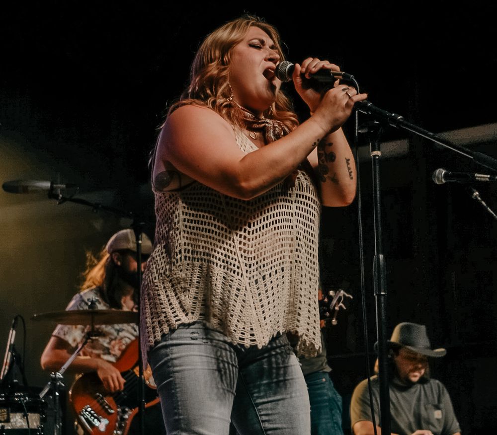 A performer sings passionately into a microphone on stage during a concert performance.