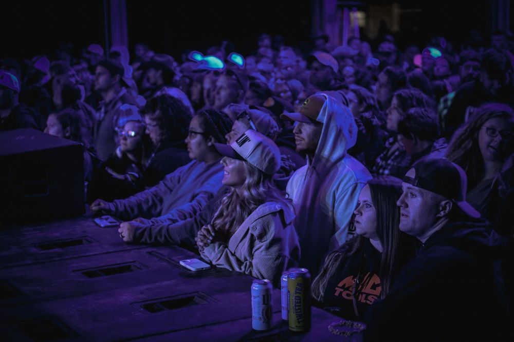 Concert audience watching performance in dark venue with blue lighting.