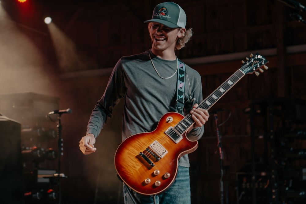 Musician playing sunburst Les Paul guitar on illuminated concert stage.