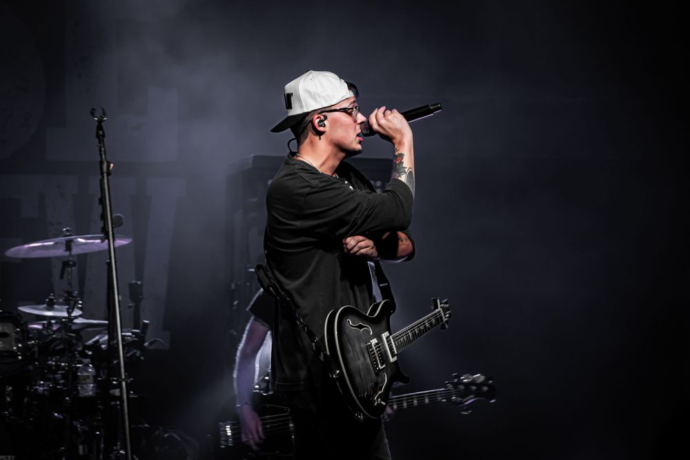 Performer singing on stage with a guitar during a concert with dramatic lighting and smoke effects.