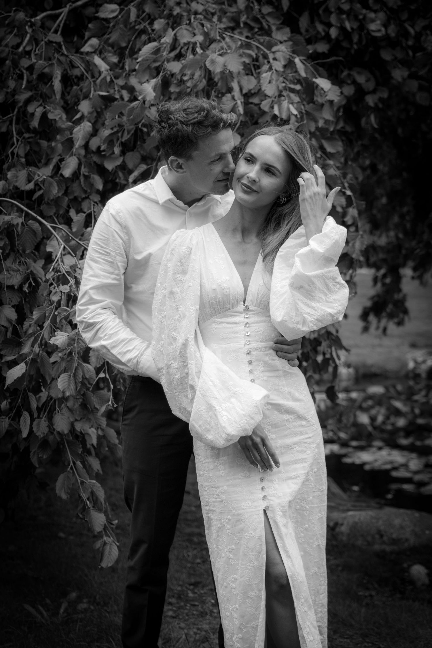 Bride and groom embracing under birch tree leaves in elegant black and white wedding portrait.