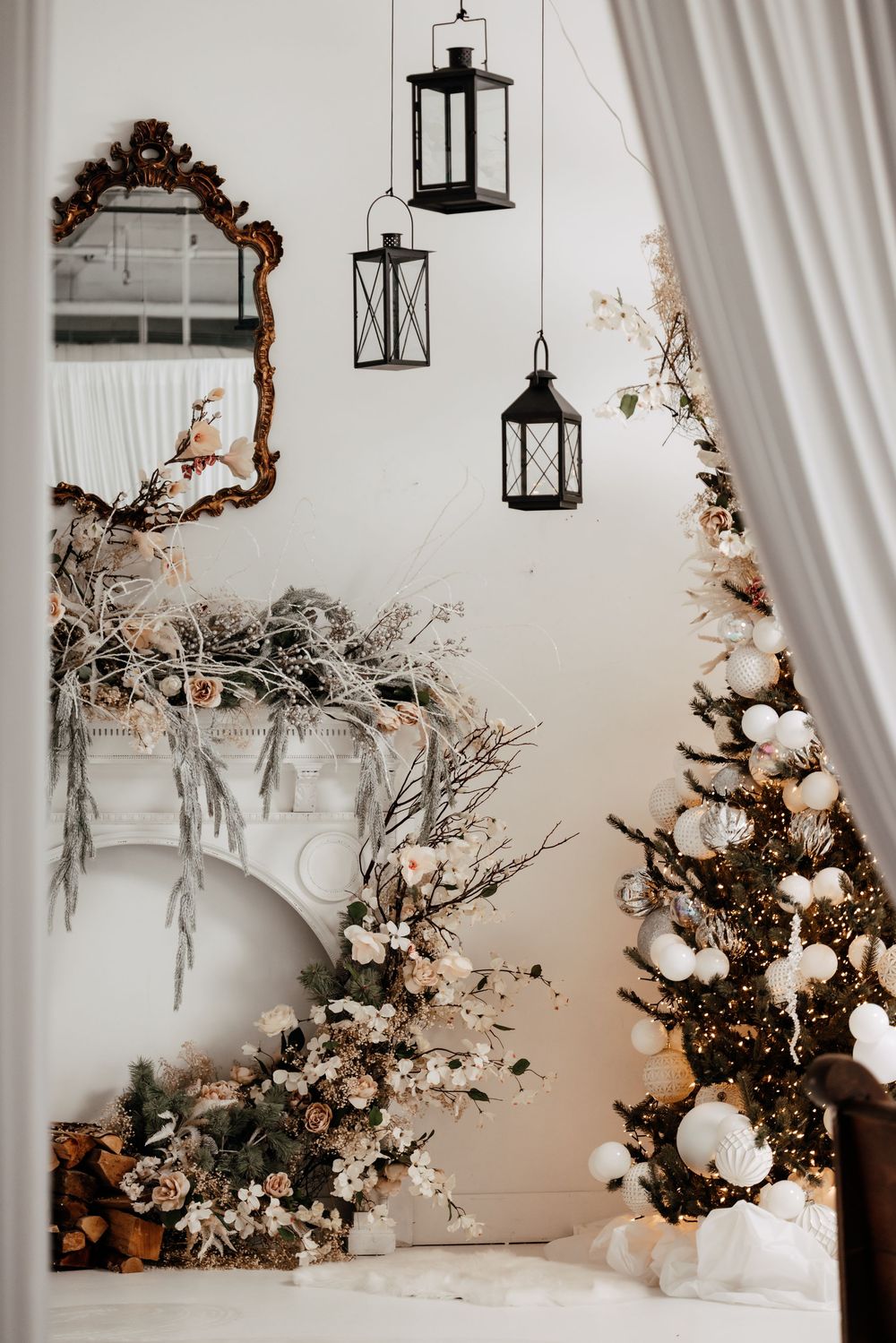 Romantic wedding decor featuring hanging lanterns, floral arrangements and draped fabric in a white space.