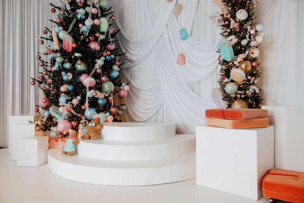 Elegant white Christmas decor with multiple decorated trees and ornate garlands in a luxurious interior setting.