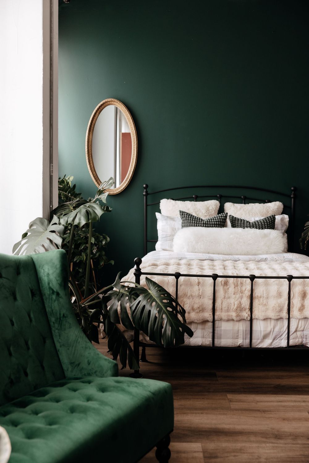 Modern bedroom interior with dark green walls, white bedding, and emerald tufted velvet seating.