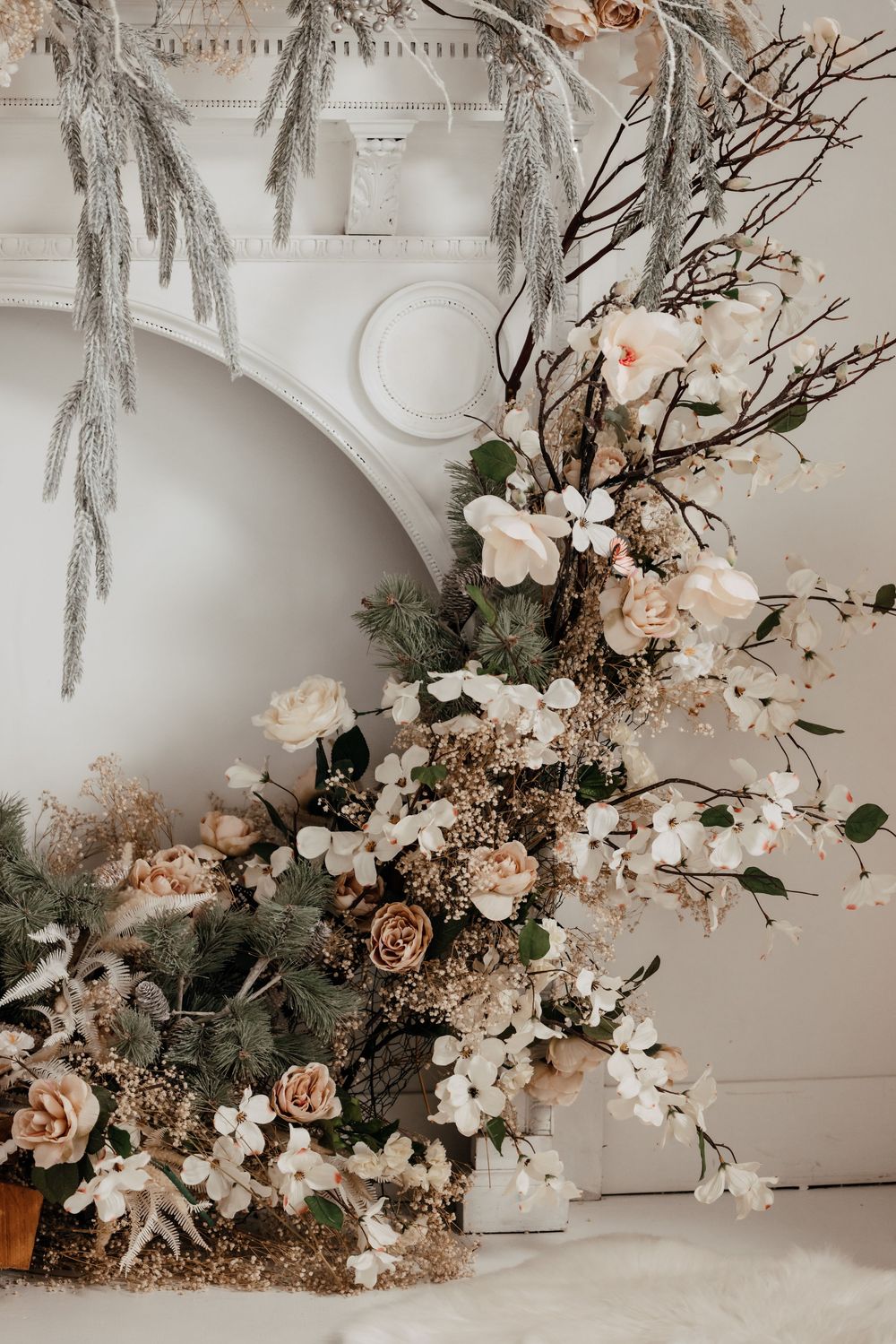Elegant floral arrangement with roses, branches and white blooms against a light neutral wall.
