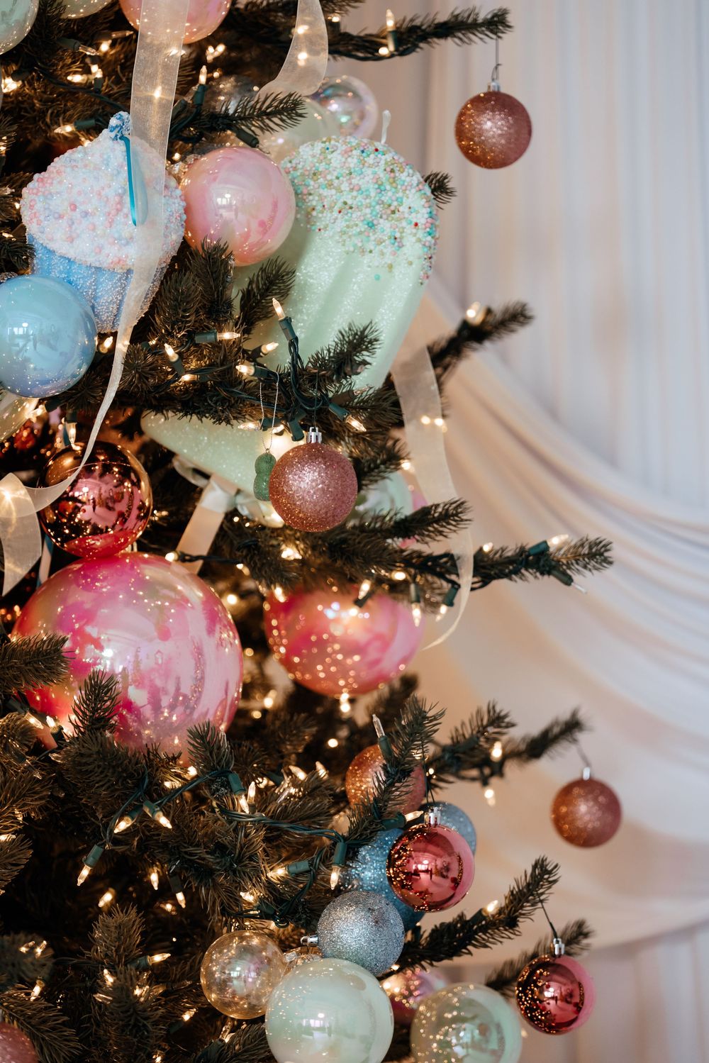 Close-up view of a Christmas tree decorated with pastel pink, blue and white ornaments and twinkling lights.