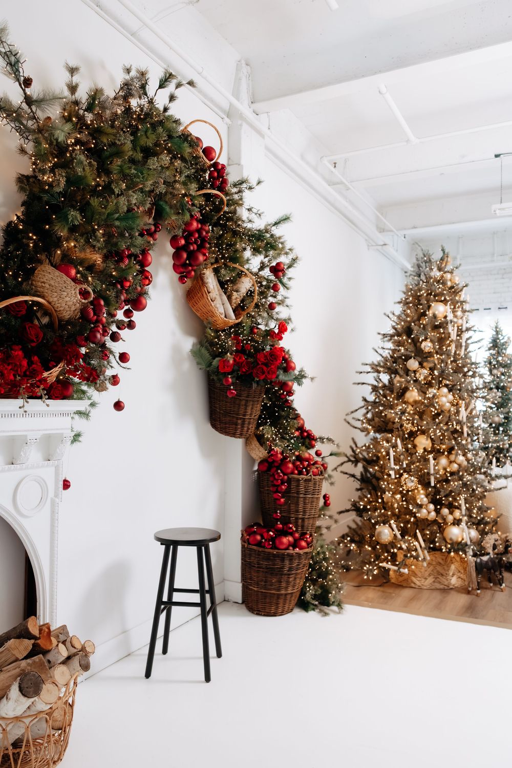 Christmas studio corner with wicker baskets of red ornaments and greenery on the wall, a black stool, and a decorated tree.