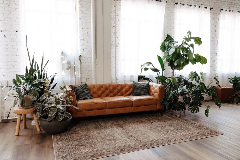 Tufted tan leather sofa on a vintage rug in a bright loft with white brick walls and lush green houseplants.