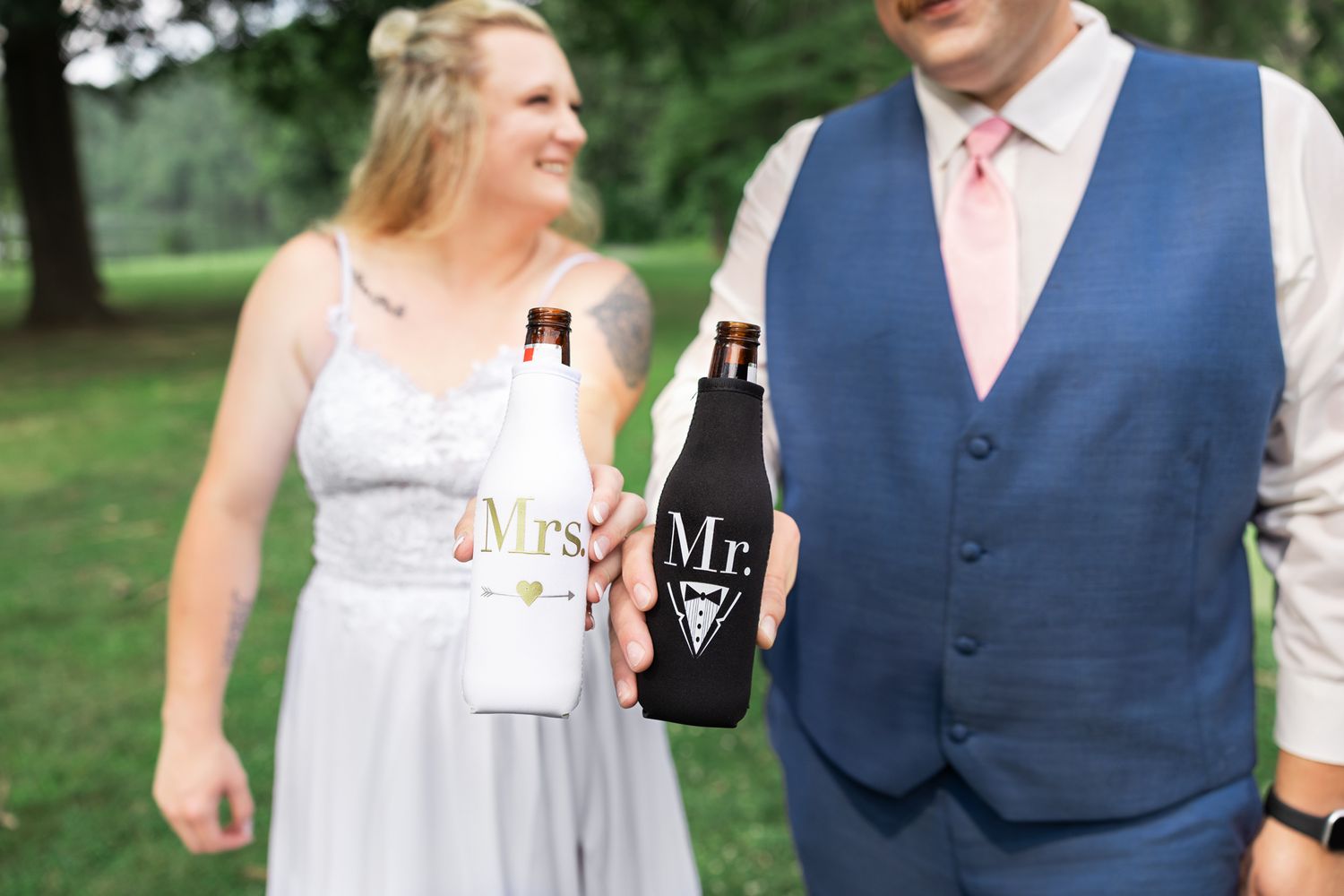 Wedding guests enjoy drinks and conversation outdoors on a sunny day while dressed in formal attire.