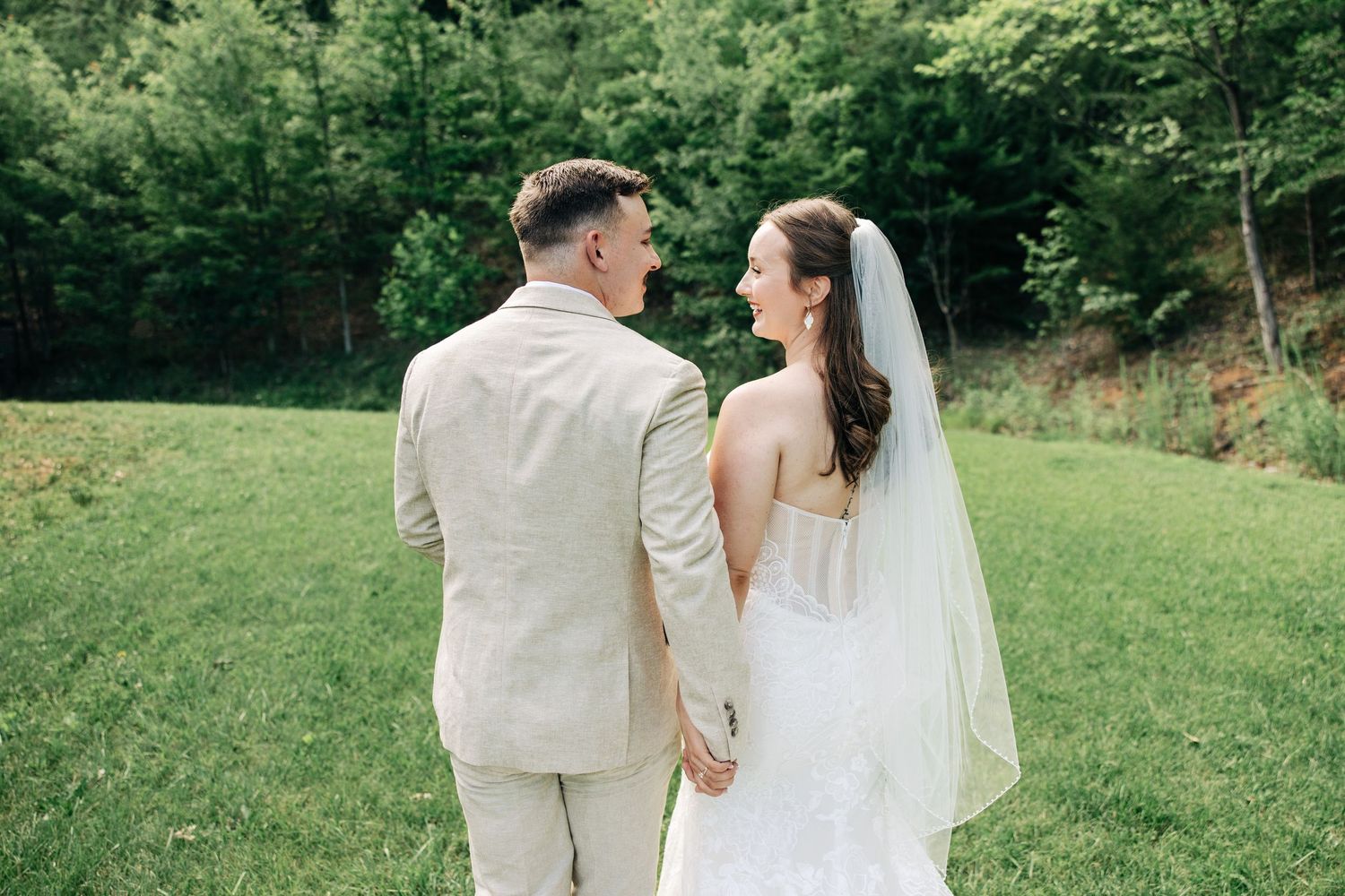 A romantic countryside wedding photoshoot with the couple walking together through lush green scenery.