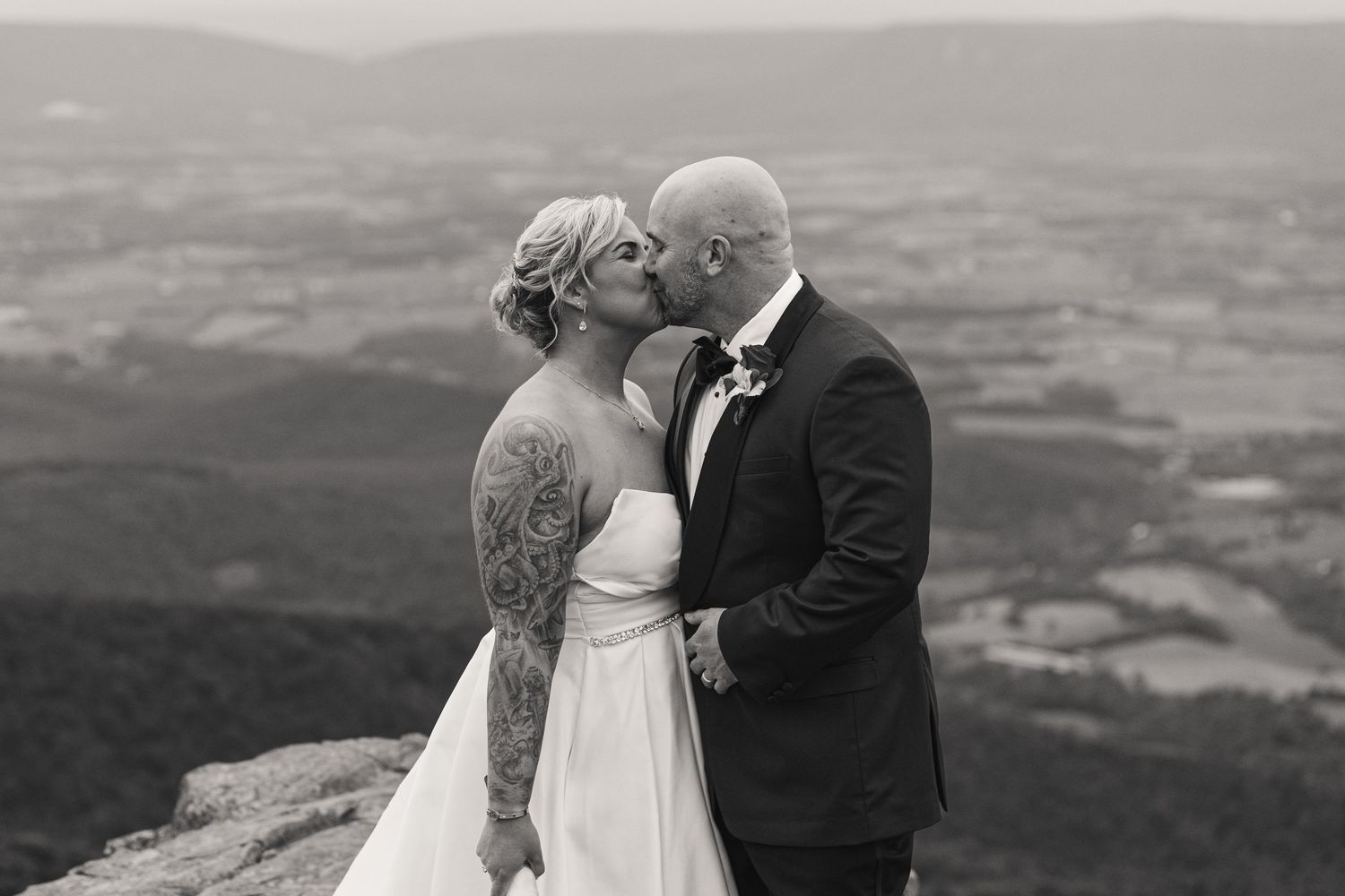 Black and white photo of a bride and groom kissing on a mountain overlook with scenic valley views.