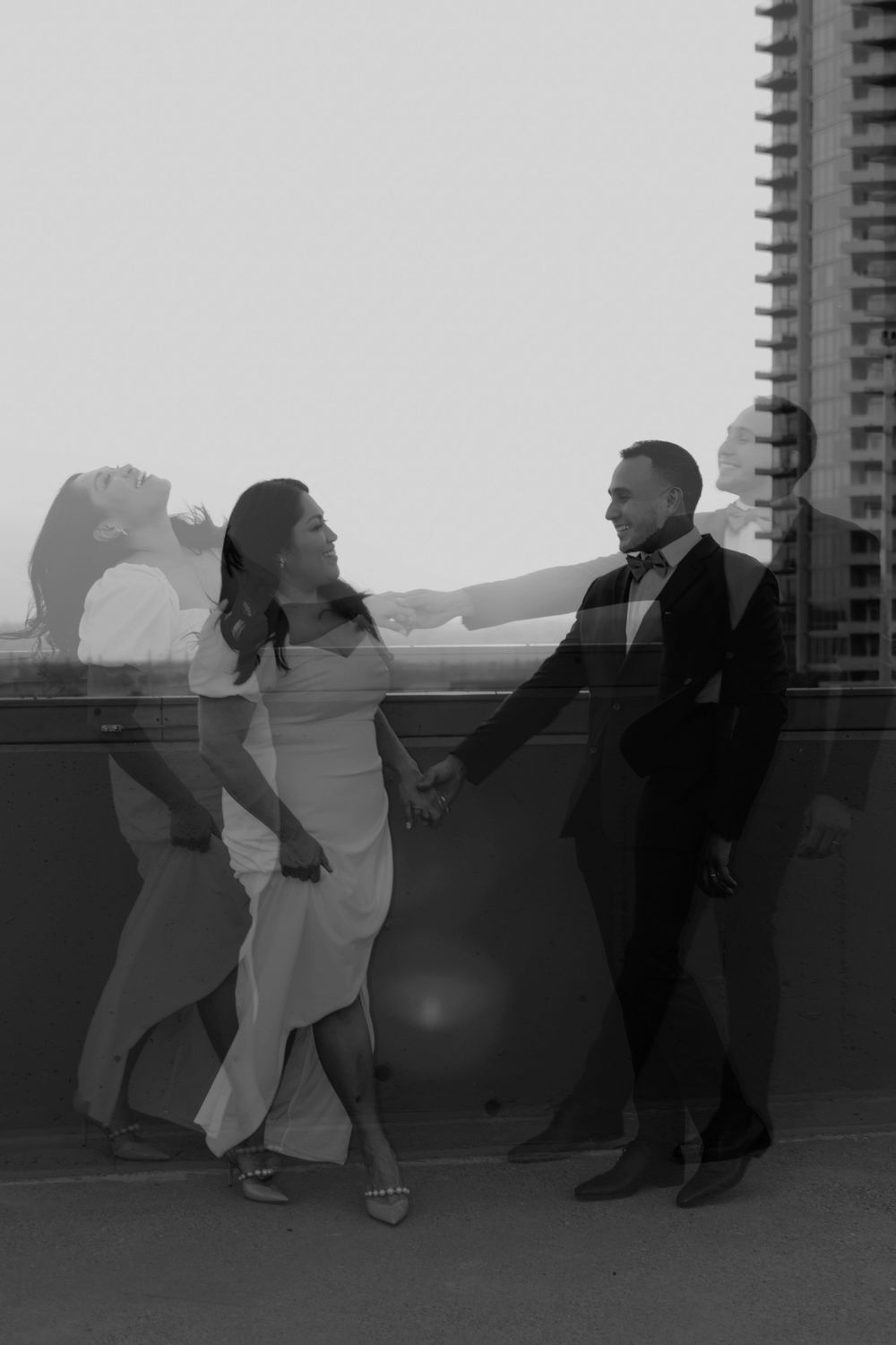 A stylish couple in formal wear dancing on a rooftop with a city skyline in black and white.