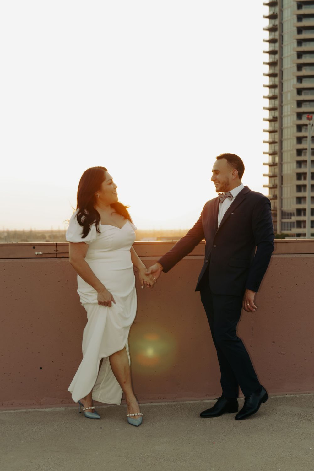 A couple in formal wear sharing a sunset moment on an urban rooftop with golden light.