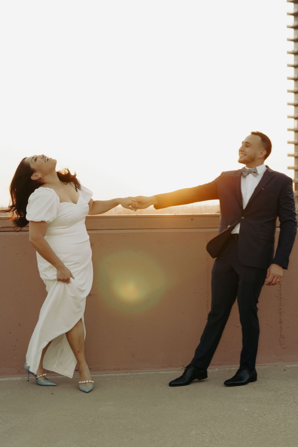 A couple dancing dramatically on a rooftop at golden hour, showing playful movement.