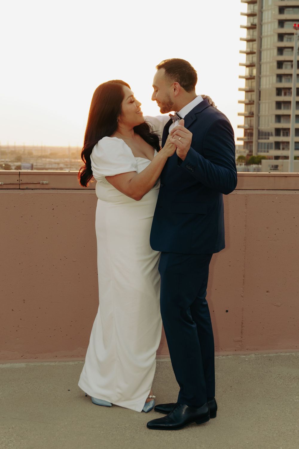 A couple in formal attire sharing an intimate dance moment on a rooftop with city views.
