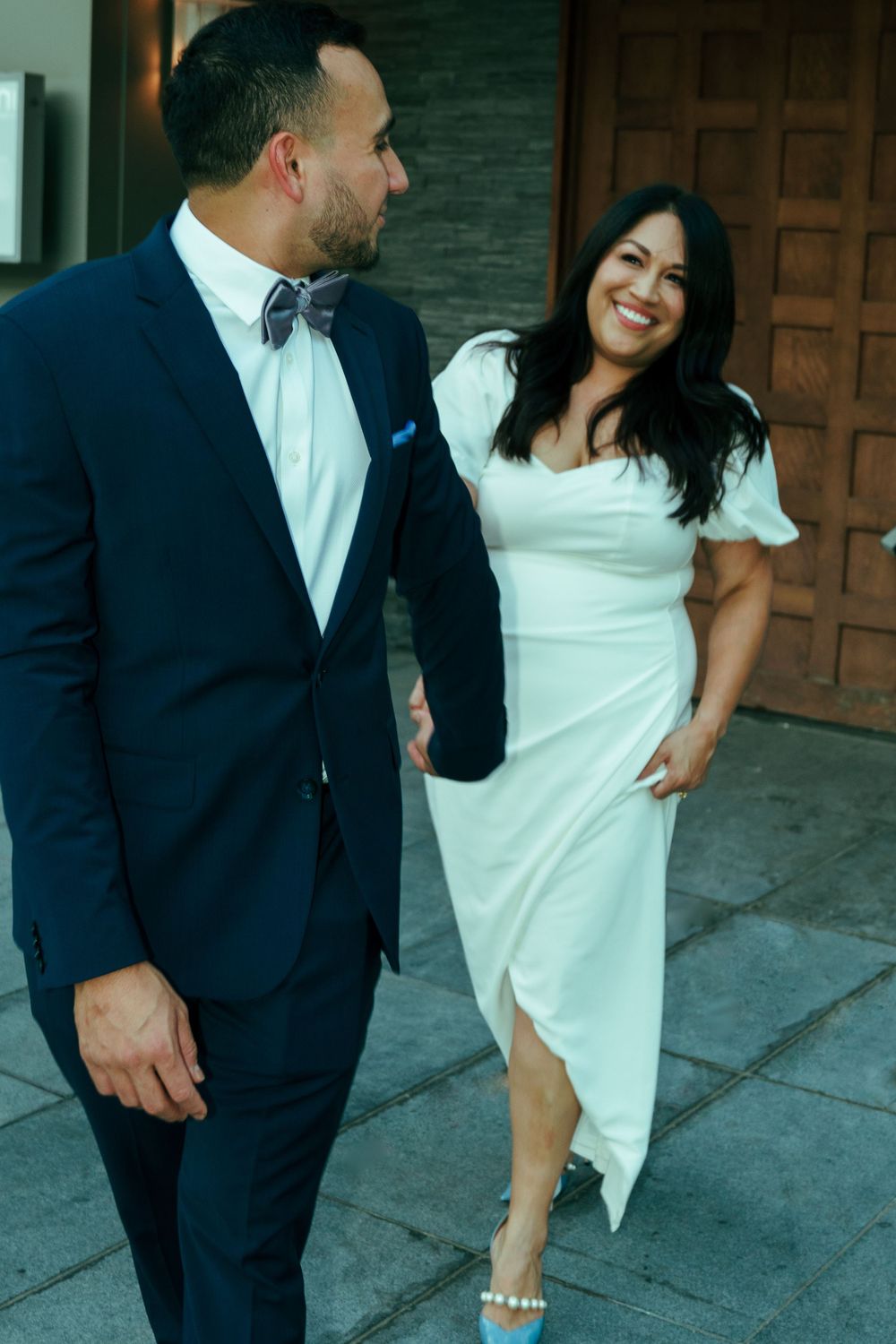 A joyful couple in formal attire sharing laughs outside a wooden door.