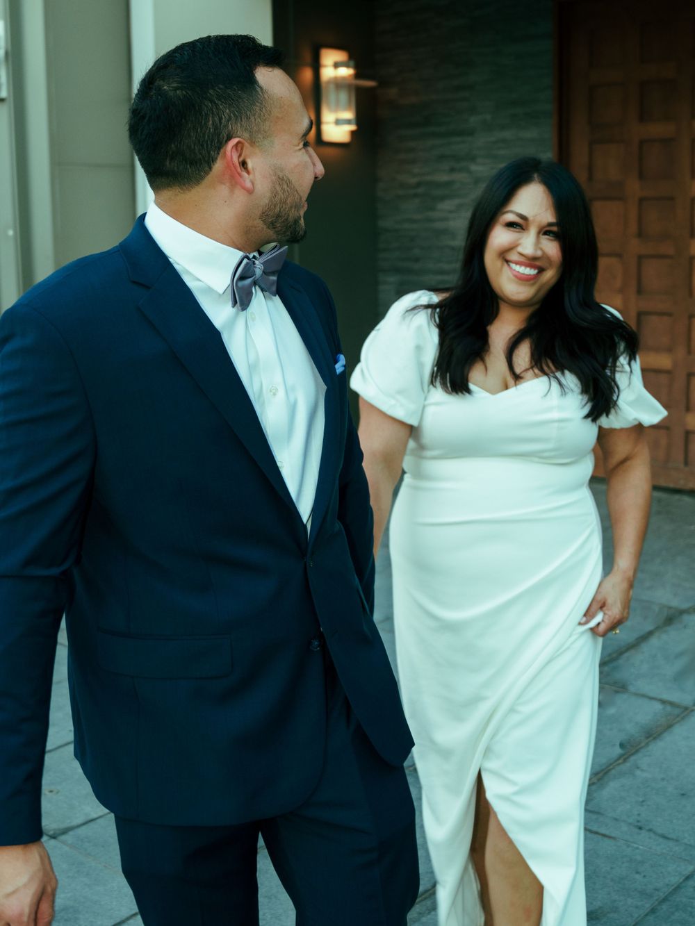 A happy couple in formal wear sharing a candid moment by a textured wall.