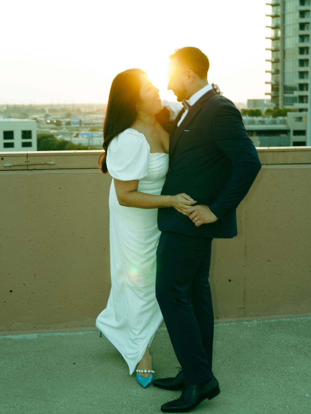 A romantic couple embracing on a rooftop at sunset with golden light behind them.