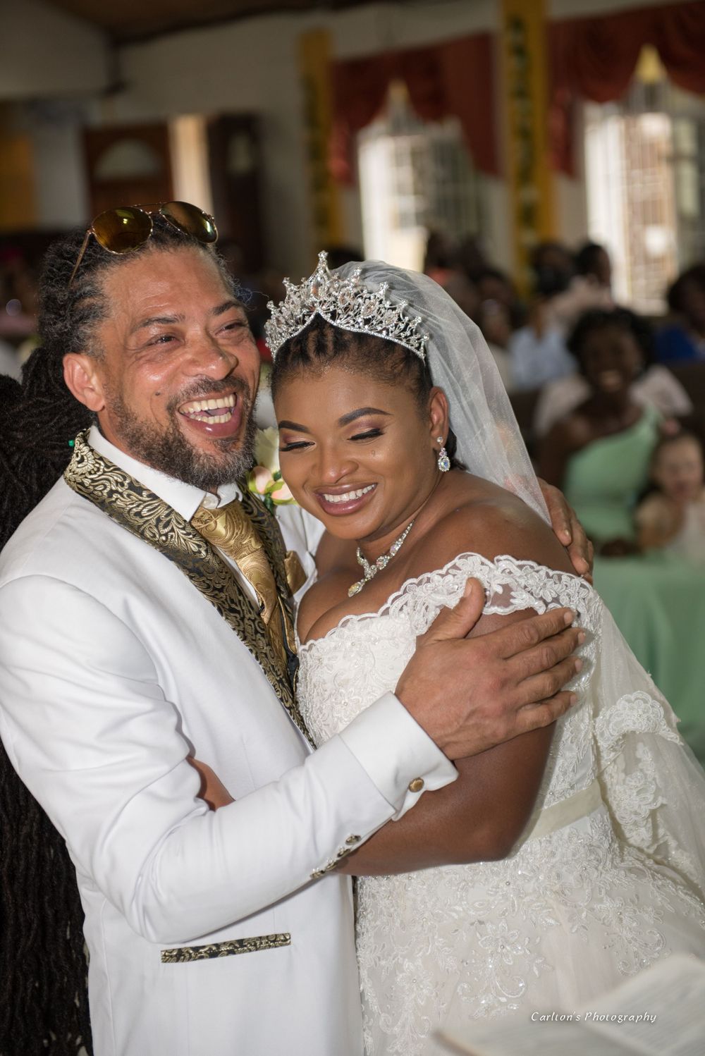 A joyful wedding couple embraces during their celebration, both wearing elegant white and gold attire.