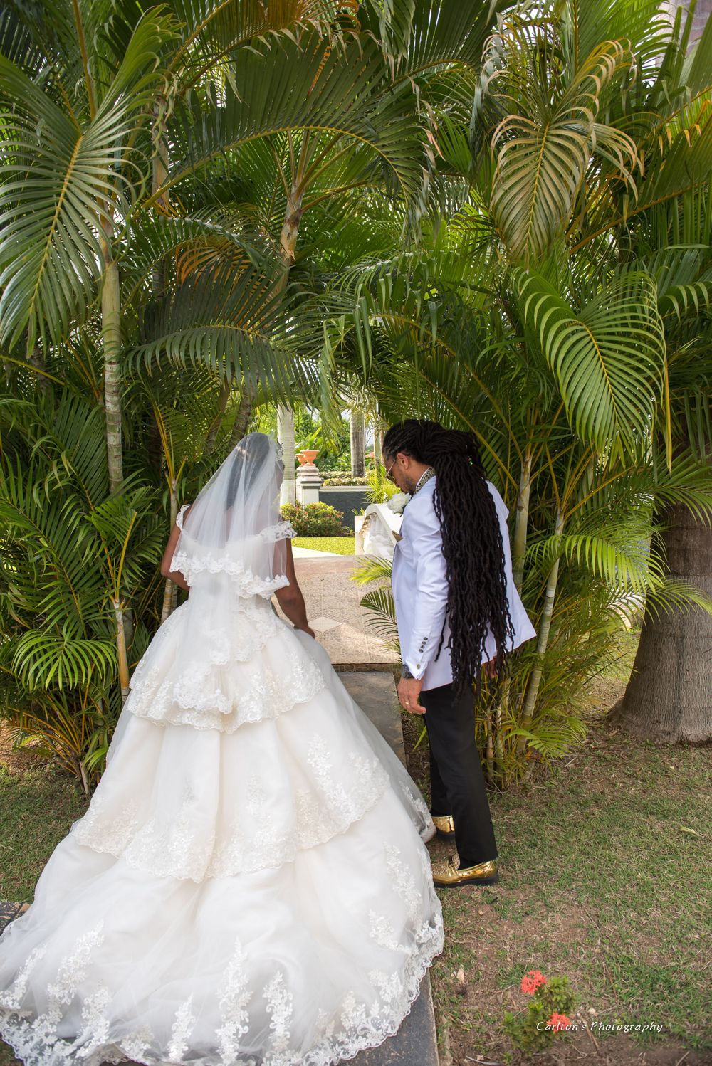 A scenic wedding portrait among tropical palm trees showing a trailing white wedding gown.