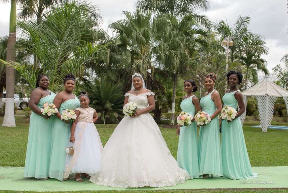 Bridesmaids in mint green dresses pose with the bride in a white gown on a lawn with palm trees.