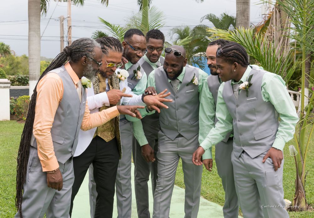 Groomsmen in gray and mint suits share a laugh while gathered on grass.