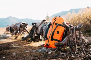 Orange hunting gear and outdoor equipment laid out on ground against mountain backdrop.