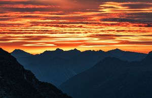Vibrant orange and red sunset sky silhouetting mountain range peaks.