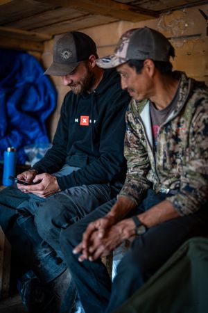 Group wearing camouflage gear relaxing in dimly lit cabin interior.