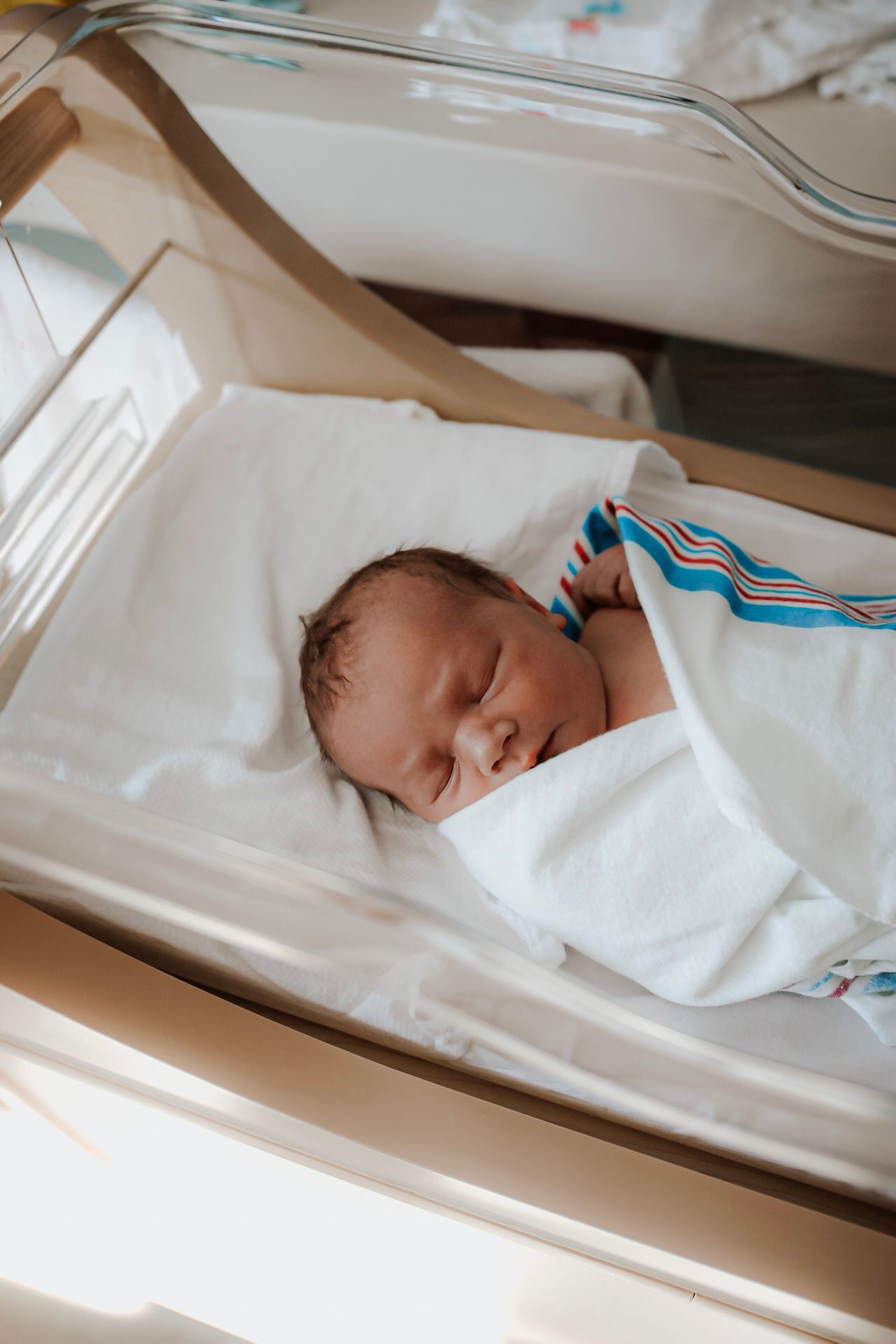 Sleeping newborn baby wrapped in white blanket during hospital photography session.