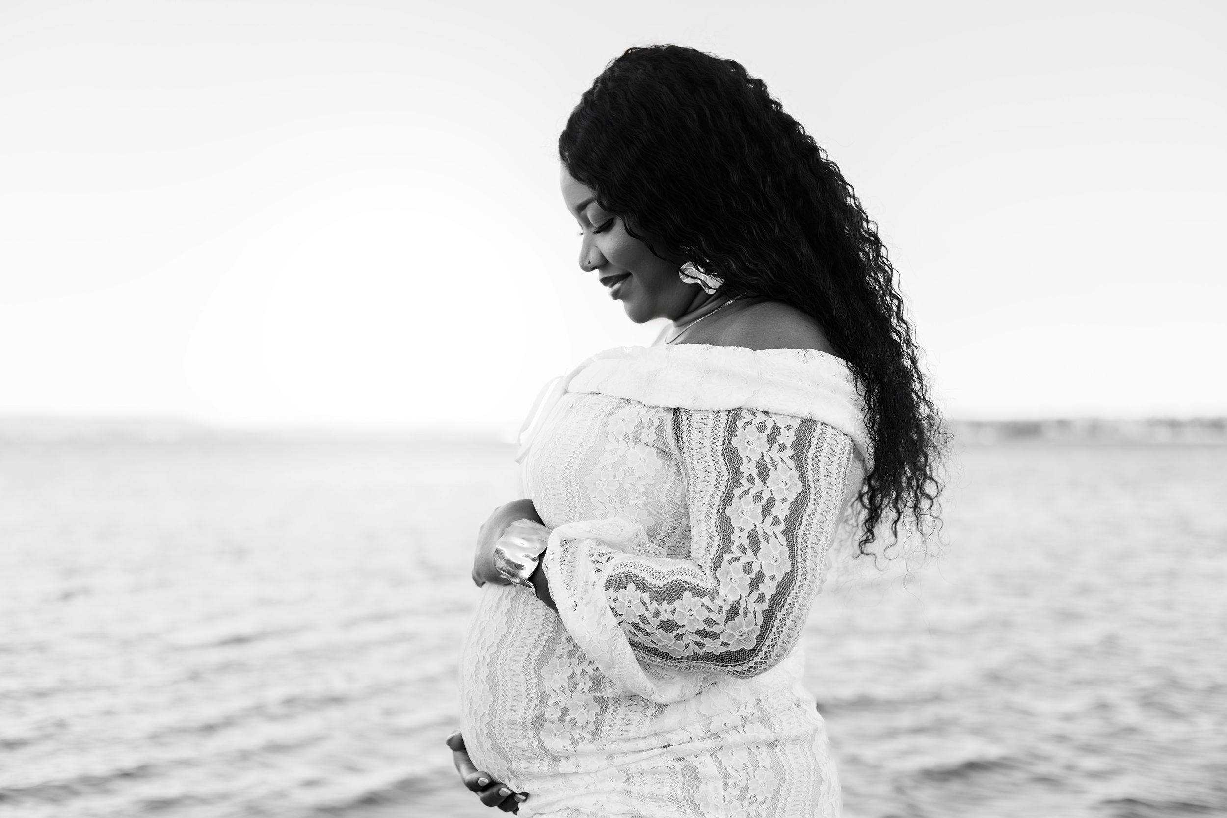 Black and white artistic beach photo series showing a woman in flowy dress sitting and walking along the shoreline.