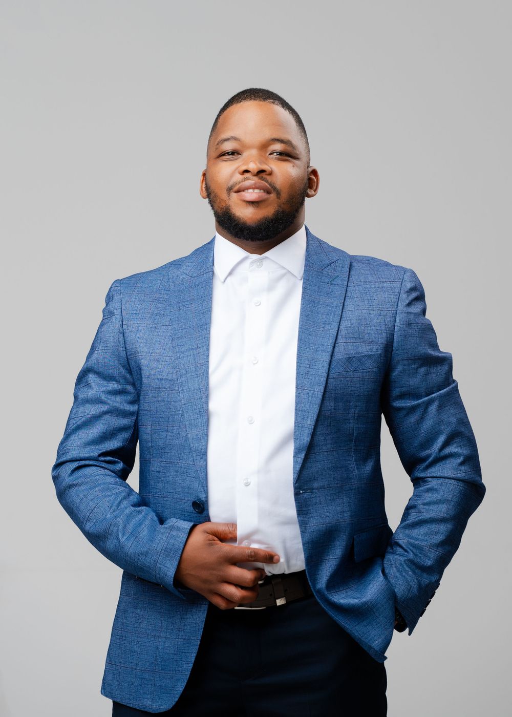 Professional wearing a tailored blue suit jacket and white dress shirt poses confidently in studio lighting.
