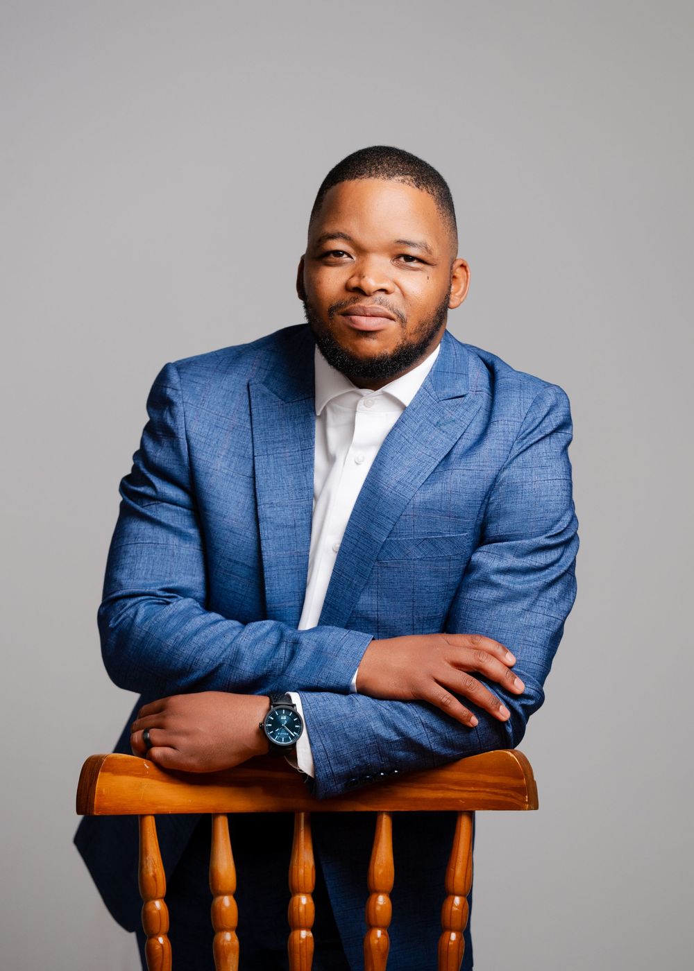 Professional portrait series of a person in a blue suit jacket posing on a wooden chair against a gray backdrop.