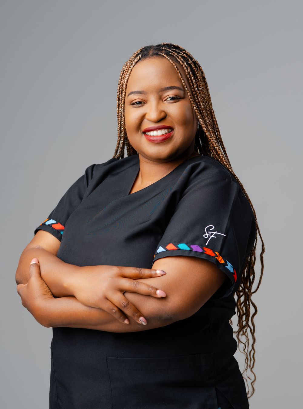 Professional portrait of someone wearing a black uniform with colorful trim, styled with long braids and a warm smile.