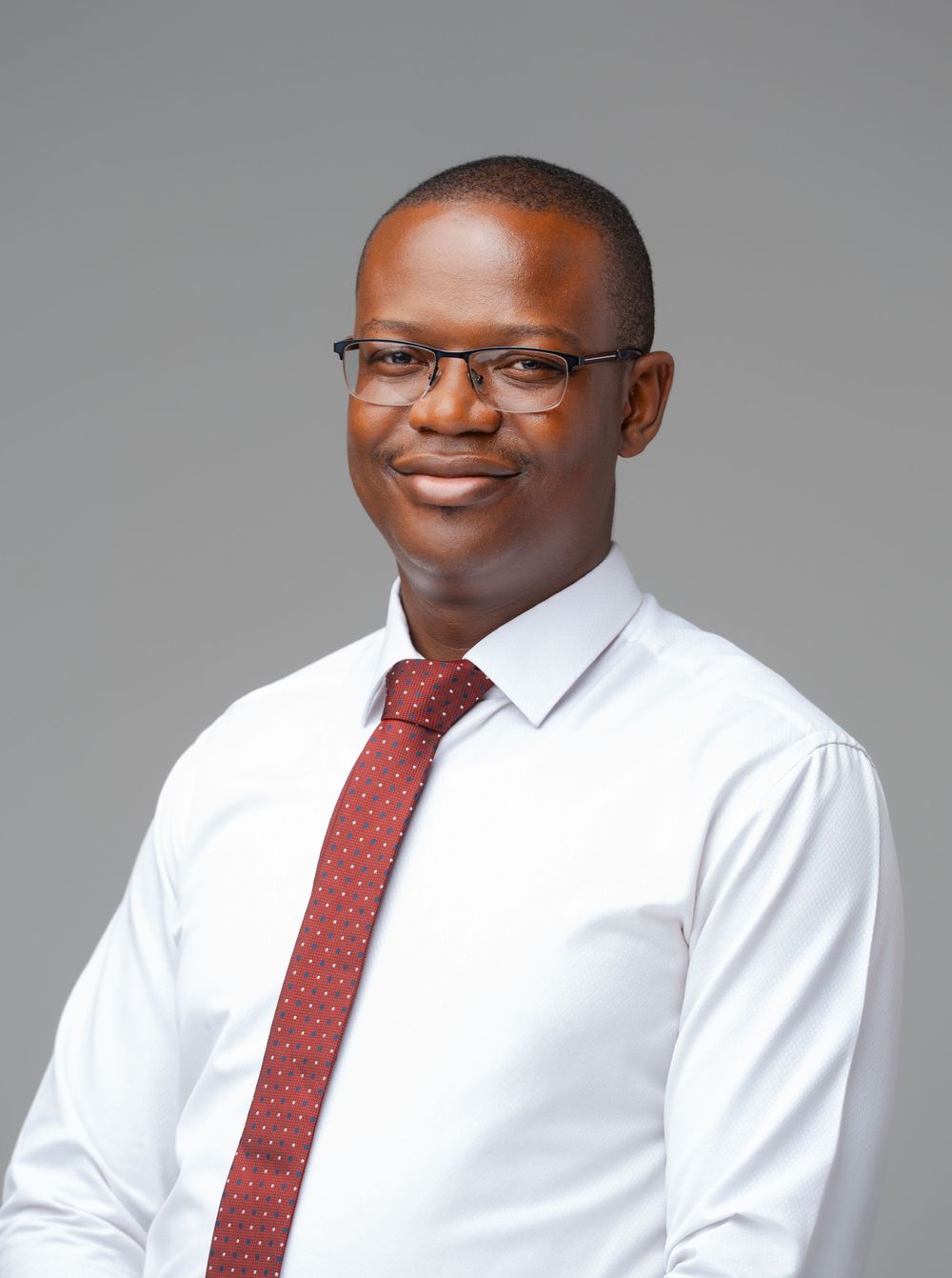 Professional headshots of someone wearing glasses, a white dress shirt and red tie against a gray background.