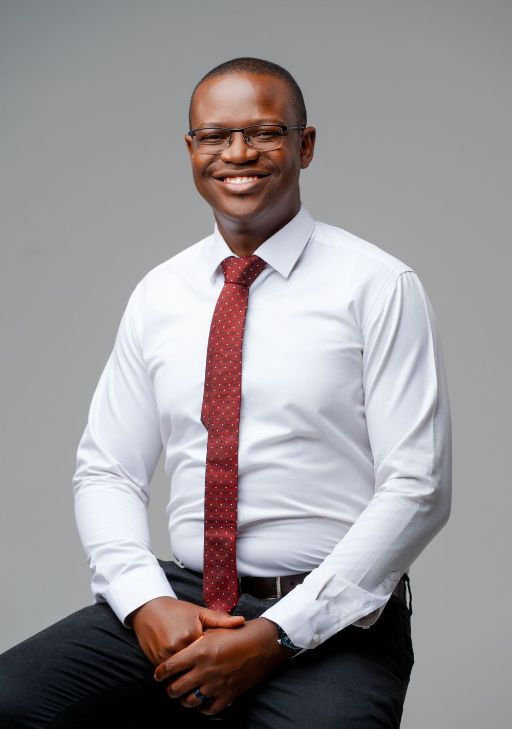 Professional business portrait of someone wearing a crisp white dress shirt and burgundy tie against a gray backdrop.