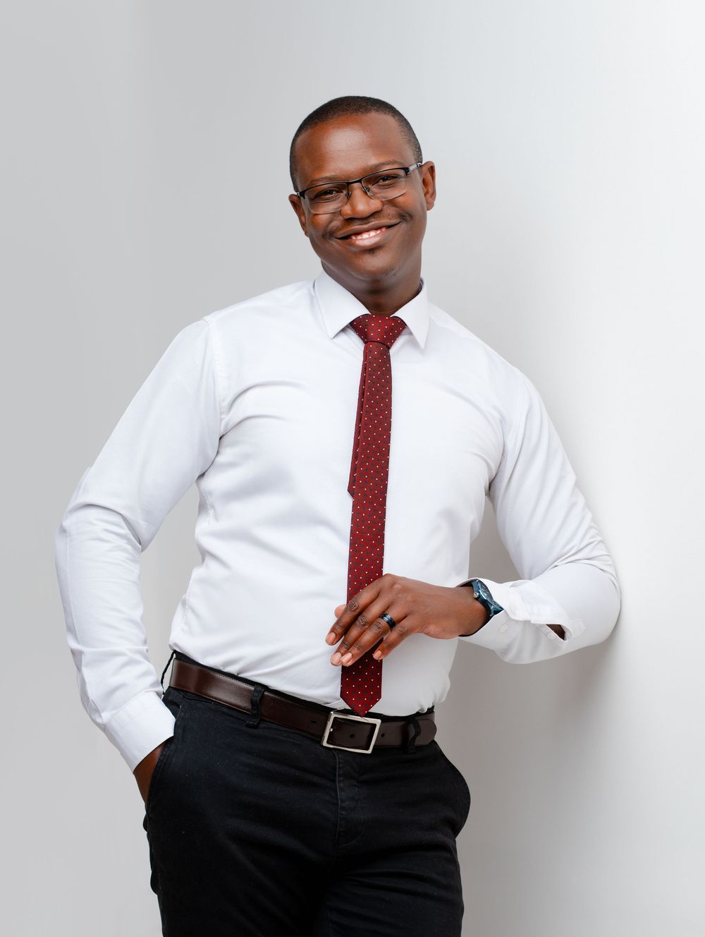 Professional wearing a white dress shirt and red polka dot tie poses confidently against a light background.