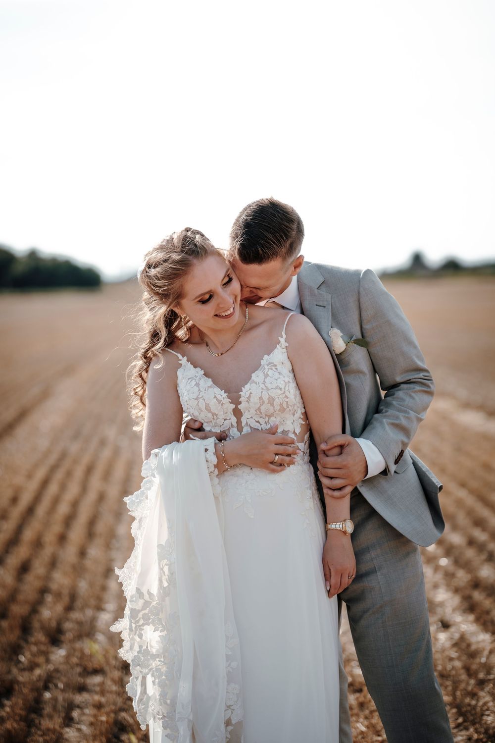 Romantic couple embraces in golden field at sunset during wedding photoshoot.